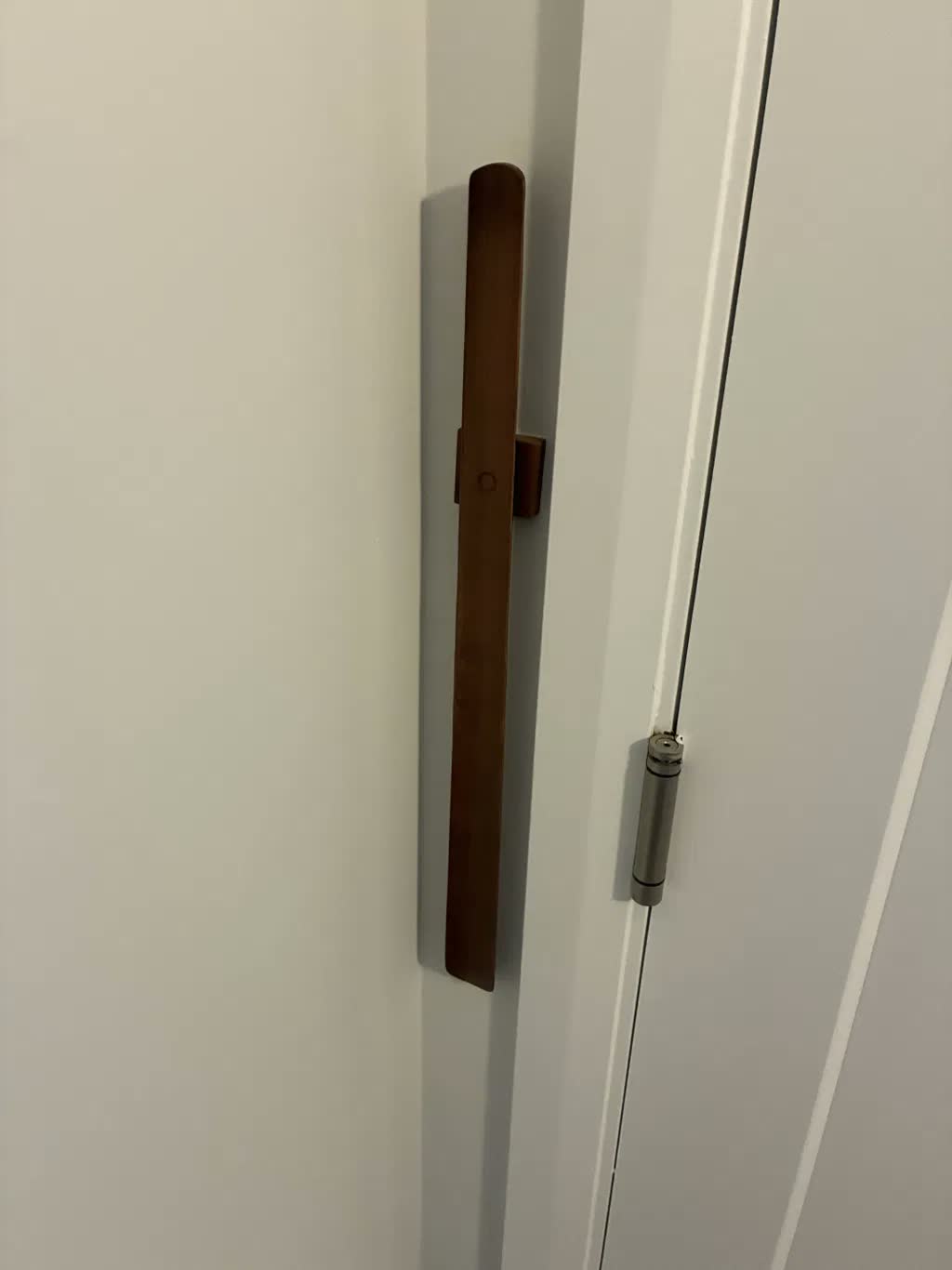 Närbild på mörkt valnötsskohorn på vit vägg bredvid vit dörr med synligt gångjärn
