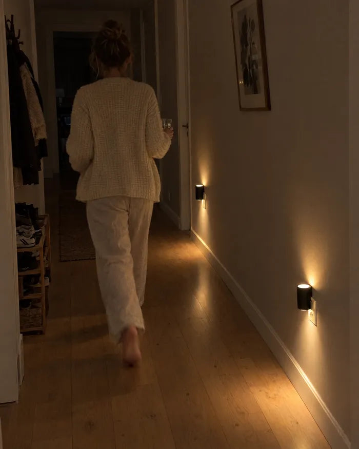 Kvinna på väg genom en mörk hall där vägglamporna lyser vid golvet